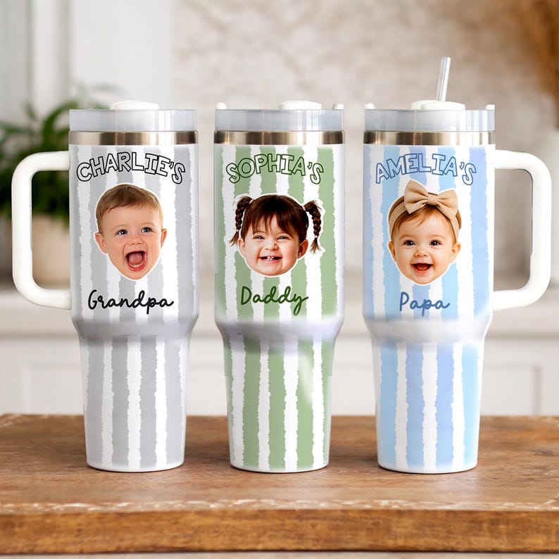 K&ouml;nnte beinhalten: Drei personalisierte Becher mit wei&szlig;en Griffen und Deckeln. Jeder Becher zeigt ein Kinderfoto und einen Namen mit dem Text "Charlie's Grandpa", "Sophia's Daddy" und "Amelia's Papa". Die Becher haben vertikal gestreifte Hintergr&uuml;nde in Grau, Gr&uuml;n und Blau.