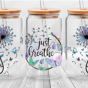 May include: Three clear glass jars with bamboo lids and straws. Each jar features a different design with a dandelion in a watercolour effect and butterflies. The middle jar has the text "Just Breathe" in a decorative font.