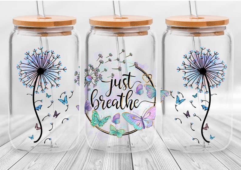 May include: Three clear glass jars with bamboo lids and straws. Each jar features a different design with a dandelion in a watercolour effect and butterflies. The middle jar has the text "Just Breathe" in a decorative font.