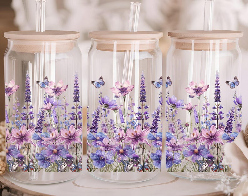 Puede incluir: Tres tarros de vidrio con tapas de madera y pajitas. Cada tarro tiene un dise&ntilde;o floral con flores y mariposas moradas, rosas y azules. Los tarros son perfectos para guardar bebidas u otros art&iacute;culos.