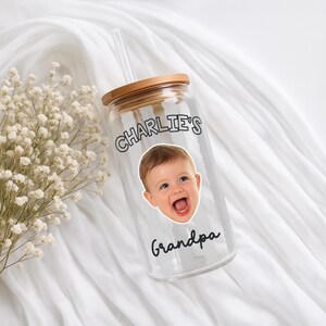 K&ouml;nnte beinhalten: Ein klares Glas mit einem Holzdeckel und einem durchsichtigen Strohhalm. Der Becher zeigt ein Foto eines Babys und die Worte "Charlie's" und "grandpa" in schwarzer Schrift. Der Becher befindet sich auf einem wei&szlig;en Hintergrund.
