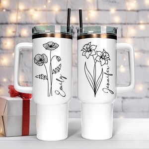 Pu&ograve; includere: Due tazze da viaggio in acciaio inox bianco con disegni floreali neri e nomi personalizzati. La tazza a sinistra ha un disegno di papavero e il nome "Emily". La tazza a destra ha un disegno di narciso e il nome "Jennifer".