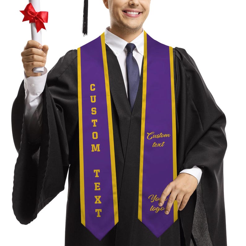 May include: A person wearing a black graduation gown and a purple and gold custom sash. The sash has the words "CUSTOM TEXT" vertically on one side and "Custom text" and "Your logo" on the other side. The person is holding a diploma.