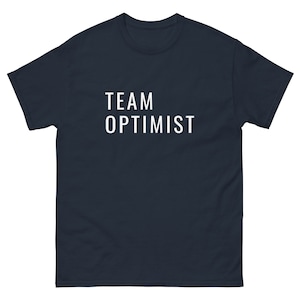 Op de afbeelding: Een marineblauw t-shirt met de tekst "TEAM OPTIMIST" in wit gedrukt op de voorkant.