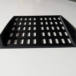 Puede incluir: Estante de rack negro con numerosas perforaciones rectangulares. El estante tiene un borde frontal ligeramente curvado y dos soportes de montaje laterales. Diseñado para equipos.