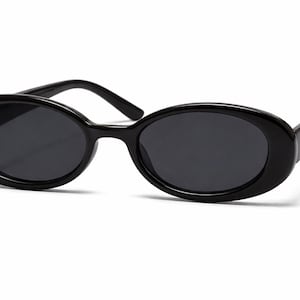 Könnte beinhalten: Schwarze ovale Sonnenbrille mit dunklen Gläsern. Die Sonnenbrille hat einen dicken, glänzenden Rahmen und ein klassisches, retro Design. Die Bügel sind gerade und erstrecken sich nach hinten.