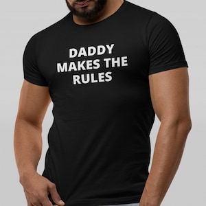 Pode incluir: Camiseta preta com texto branco que diz "Daddy Makes The Rules".