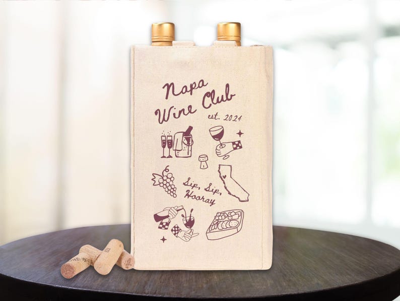 May include: A beige canvas wine tote bag with the text "Napa Wine Club est. 2024" printed in maroon. The bag features illustrations of wine bottles, glasses, grapes, and a map of California.