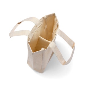 May include: A beige canvas tote bag with two separate compartments. The bag has two handles and is open at the top.