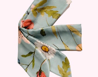 May include: Two light turquoise fabric hair scrunchies with a floral print featuring small pink, white, and yellow flowers and green leaves. The scrunchies are 34 inches long.