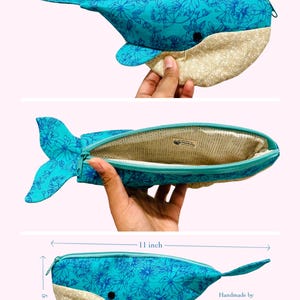 以下が含まれることがあります： 花柄のティールブルーとサンドベージュの腹部を持つ、クジラの形をしたペンケース。ジッパー開閉式で、長さ27.94cm、高さ12.7cmです。内側は明るい色の生地で裏打ちされています。