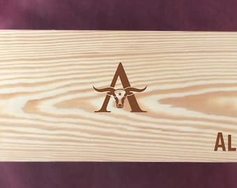 May include: A wooden box with a brown, engraved design of a longhorn steer head inside the letter "A" and the name "ALEX" below.