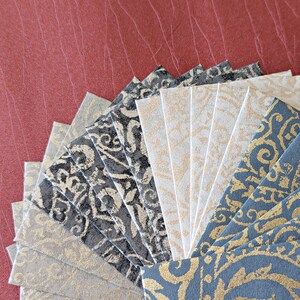 May include: A fan of patterned paper in various shades of gray and gold. The paper is arranged in a semi-circle with the darker shades on the outside and the lighter shades on the inside.