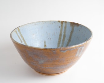 May include: A large, brown ceramic bowl with a light blue glaze. The bowl has a slightly irregular shape and a textured surface.