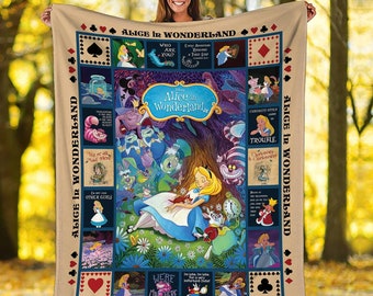 May include: A beige fleece blanket with a patchwork design featuring scenes from Alice in Wonderland. The center panel shows Alice sleeping under a tree with the Cheshire Cat, Mad Hatter, and other characters. The surrounding panels feature various quotes and scenes from the story, including "We're all mad here", "Curiosity often leads to trouble", and "Who are you?"