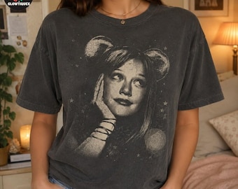 May include: A charcoal grey short-sleeve t-shirt featuring a distressed, monochromatic graphic print of a person with mouse ears, surrounded by small stars. The shirt has a crew neckline and a relaxed fit, showcasing a vintage-inspired aesthetic.