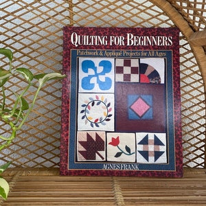 May include: A book titled "Quilting for Beginners" with patchwork and appliqué projects for all ages. The cover displays a burgundy background with various quilt block designs in blue, red, and brown. The author's name, Agnes Frank, is at the bottom.