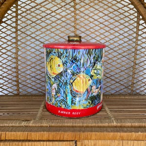 May include: A cylindrical tin with a red lid and base, featuring a colourful underwater scene with yellow fish and coral. The words "BARRIER REEF" are printed on the base. The tin is approximately 15 cm tall.
