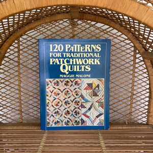 May include: A book titled "120 Patterns for Traditional Patchwork Quilts" by Maggie Malone. The book has a blue cover with colourful quilt patterns. The book is displayed on a woven wicker shelf.
