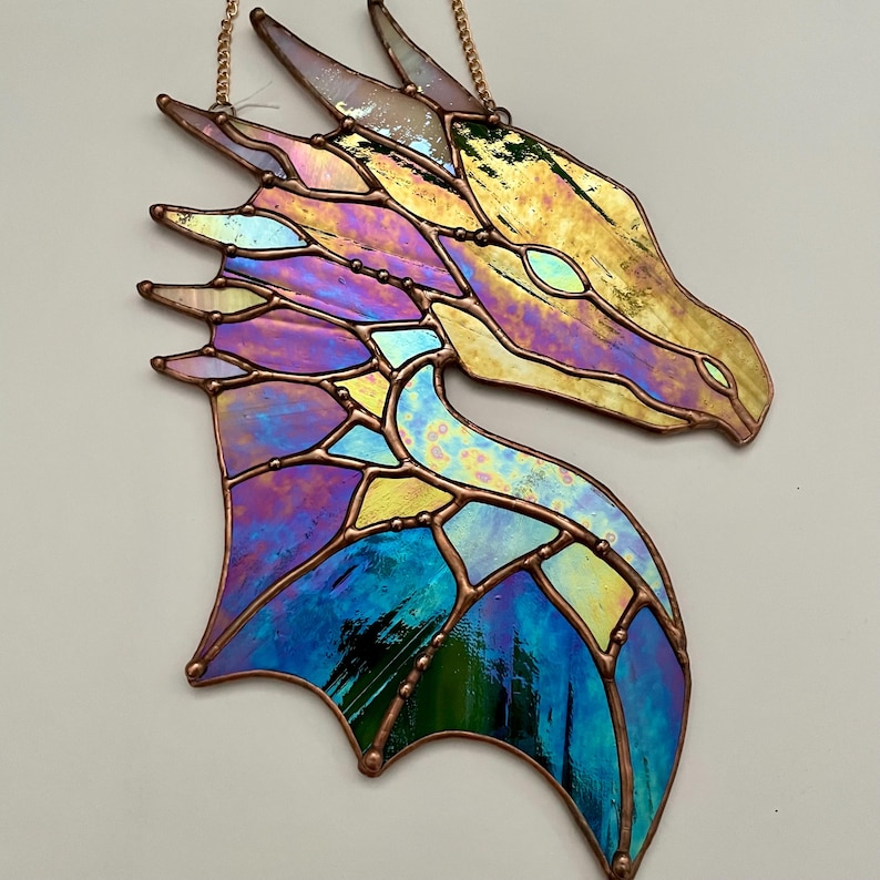 May include: A stained glass dragon head with iridescent blue, purple, and yellow glass. The dragon head is hanging from a gold chain.