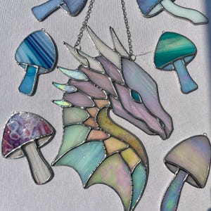May include: A stained glass dragon head with iridescent wings and a pastel color scheme. The dragon is surrounded by stained glass mushrooms in various colors, including blue, green, purple, and white.