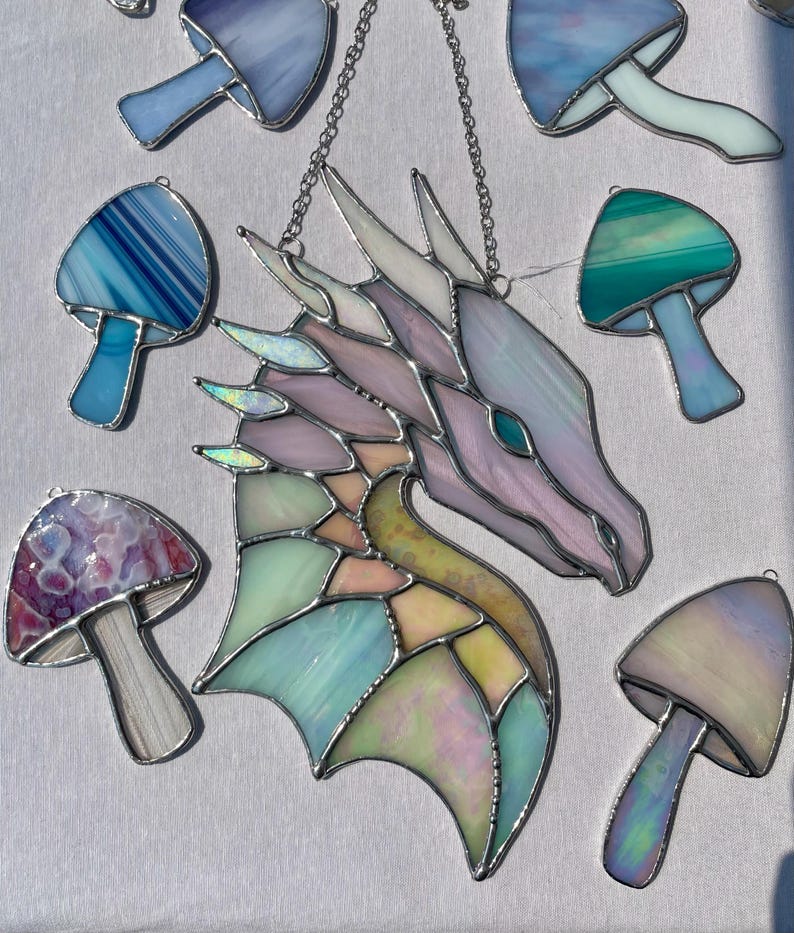 May include: A stained glass dragon head with iridescent wings and a pastel color scheme. The dragon is surrounded by stained glass mushrooms in various colors, including blue, green, purple, and white.