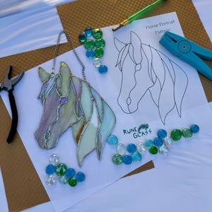 May include: A stained glass horse head with a silver chain, featuring pastel colors. A printed horse portrait pattern, glass beads, and tools are arranged around the artwork. The text "Rune Glass" is visible.