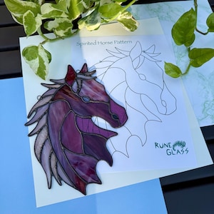 Op de afbeelding: Een gebrandschilderd glazen paardenkop in tinten paars, rood en lavendel, met een gedetailleerd omtrekpatroon op een wit vel. De teksten "Spirited Horse Pattern" en "Rune Glass" zijn zichtbaar. Het kunstwerk staat tegen een blauwe en zwarte achtergrond.