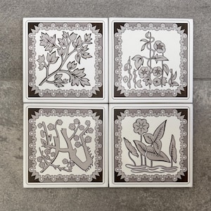 May include: Four square ceramic tiles with floral designs. Each tile features a different botanical illustration in shades of grey and white, framed by a decorative border. The tiles are arranged in a 2x2 grid.