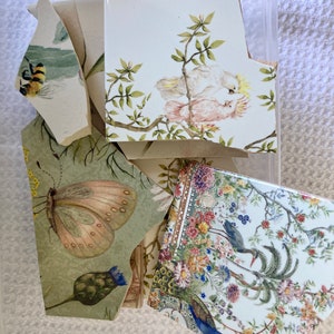 May include: A collection of ceramic tiles featuring floral and bird designs. The tiles are decorated with a variety of colours, including white, green, pink, blue, and yellow. The designs include a butterfly, a peacock, a pair of cockatoos, and a variety of flowers.