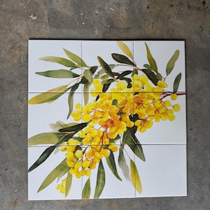 May include: Nine white ceramic tiles arranged in a square, depicting a watercolour painting of yellow wattle flowers and green leaves. The floral design is centred on the tiles, creating a decorative pattern.