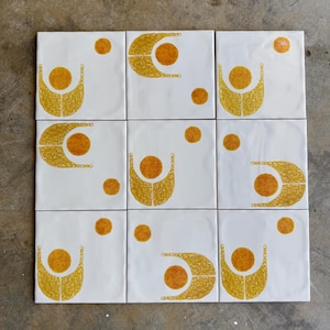 May include: Nine white ceramic tiles with a geometric pattern of yellow and orange circles and arcs. The tiles are arranged in a 3x3 grid.