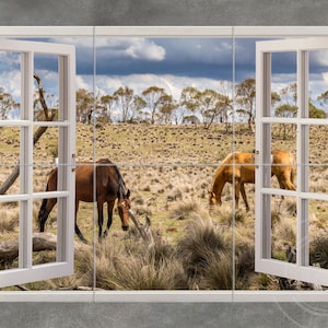 May include: A picturesque scene of two horses grazing in a field, viewed through a white window. One horse is brown, the other is tan. The landscape features dry grass, trees, and a cloudy sky.