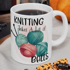 May include: White ceramic coffee mug with a black handle. The mug has a graphic of yarn balls and knitting needles with the text "Knitting Takes A Lot of Balls".