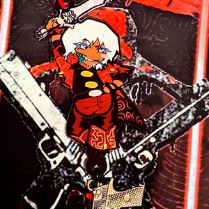 May include: A double-sided acrylic charm featuring a stylized character with white hair, a red coat, and a rose in their mouth, holding a sword. A red star-shaped clasp is attached to the top, and a small gold-colored handgun charm hangs below.