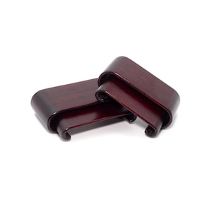 May include: Two dark red wooden display stands. Each stand has a rectangular base with curved, scrolled ends. The wood grain is visible, and the stands are designed to elevate small objects.
