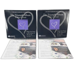 Könnte beinhalten: Zwei schwarze Fotoalben mit dem Titel "The Triumph Album" und einem lila Herzdesign. Die Alben tragen den Text "Keep your heart at the center of all you do." Das Logo der Creative Memories Collection ist sichtbar.