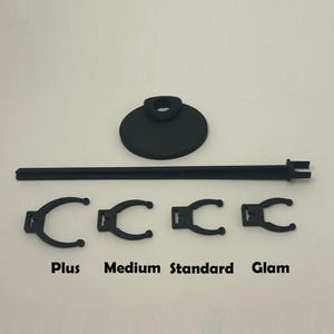 May include: Black display stand with a round base and a horizontal bar, plus four black clips labelled "Plus", "Medium", "Standard", and "Glam". The stand is designed to hold items for display.