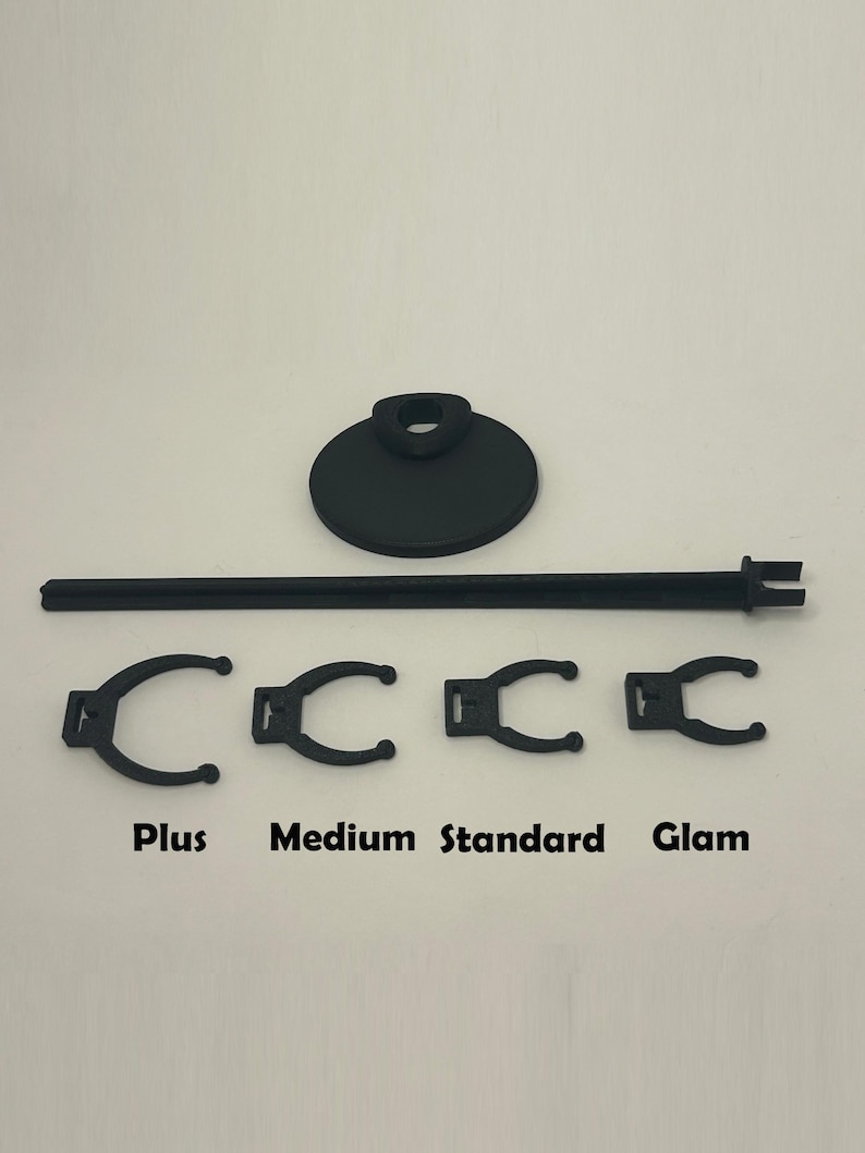May include: Black display stand with a round base and a horizontal bar, plus four black clips labelled "Plus", "Medium", "Standard", and "Glam". The stand is designed to hold items for display.
