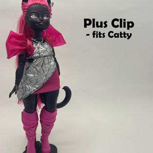 May include: A black doll with pink hair, a silver and pink dress, and pink boots. The doll has cat-like features and is standing on a black base. Text on the image reads "Plus Clip - fits Catty."