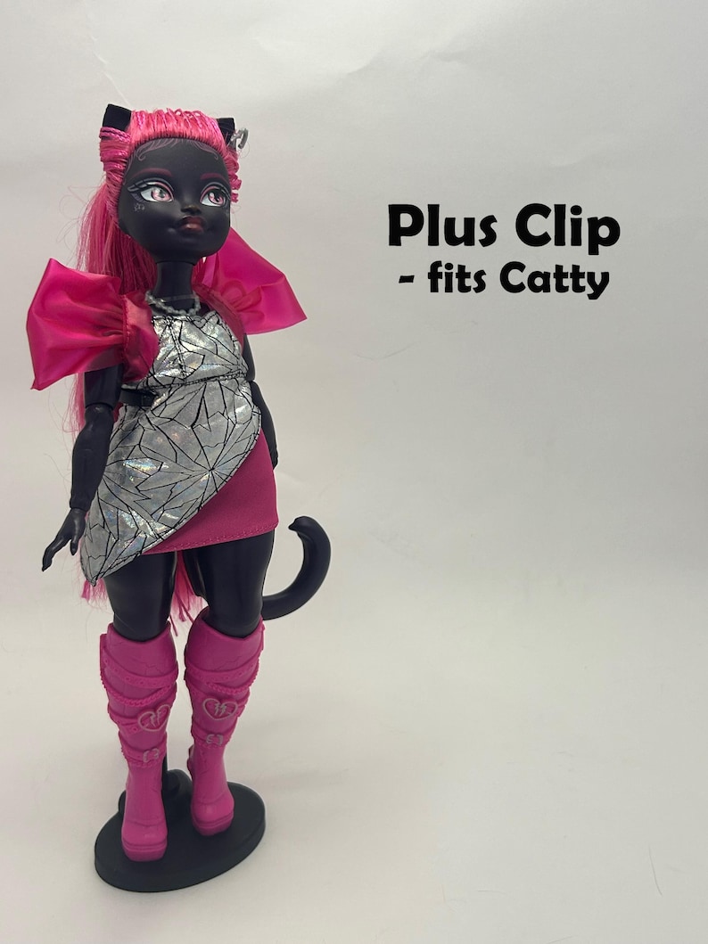 May include: A black doll with pink hair, a silver and pink dress, and pink boots. The doll has cat-like features and is standing on a black base. Text on the image reads "Plus Clip - fits Catty."