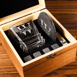 Puede incluir: Una caja de madera con un vaso de whisky de vidrio, un posavasos de pizarra y piedras de whisky. El vaso y el posavasos est&aacute;n grabados con el nombre "William".