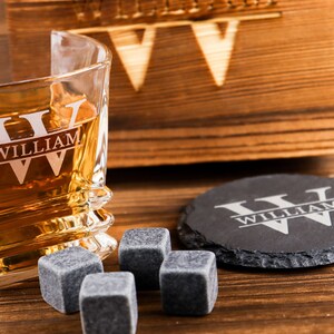 Puede incluir: Un juego de vasos de whisky personalizado con una caja de madera, un posavasos de pizarra y cuatro piedras de whisky. El vaso y el posavasos est&aacute;n grabados con el nombre "William" y las iniciales "W" en un estilo de monograma dividido.