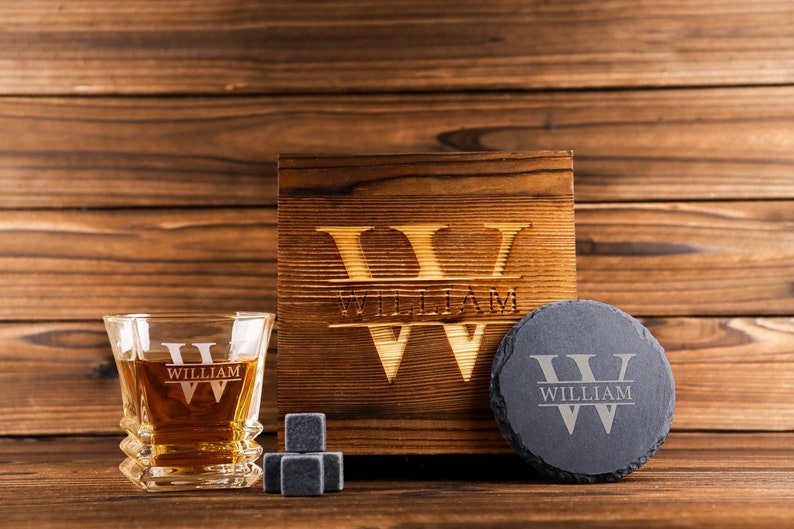 Puede incluir: Un set de regalo de whisky personalizado con una caja de madera, un vaso, un posavasos de pizarra y piedras de whisky. La caja, el vaso y el posavasos est&aacute;n grabados con el nombre "William" y la letra "W".