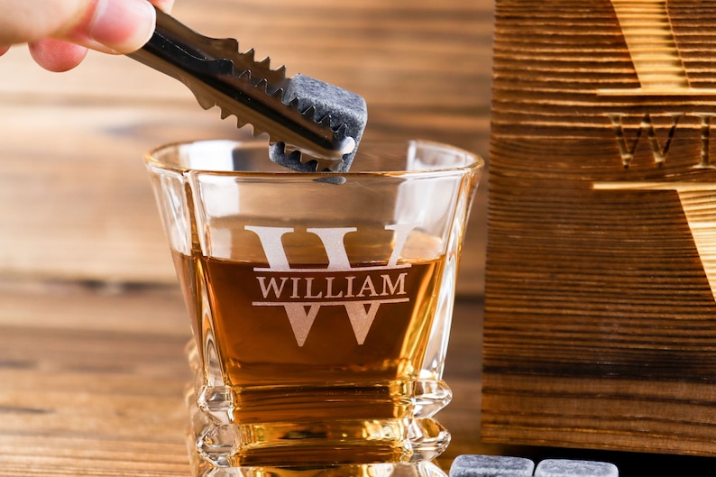 Puede incluir: Un vaso de whisky personalizado con el nombre "William" grabado en &eacute;l. El vaso est&aacute; lleno de l&iacute;quido &aacute;mbar y se coloca una piedra de whisky en el vaso con unas pinzas.