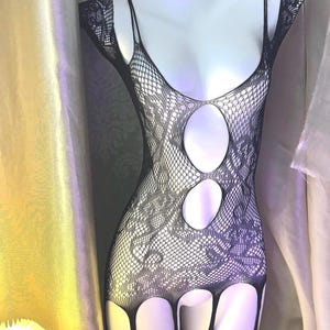May include: Black fishnet body stocking with a floral pattern and cut-out design. The lingerie features thin straps and cut-outs at the chest and legs. The garment is displayed on a white mannequin.