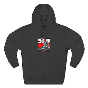 May include: Dark gray hoodie with a front pocket and hood. The graphic on the front features a red sun, Japanese text, and a cartoon of a monster on top of a car.