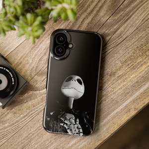 Puede incluir: Funda de teléfono negra con una ilustración en escala de grises de Jack Skellington de Pesadilla antes de Navidad. El diseño incluye su rostro esquelético, cuello y parte de su traje. La funda está sobre una superficie de madera.