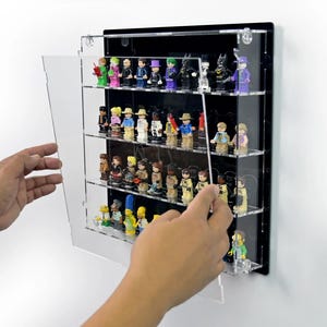 Puede incluir: Una vitrina de acrílico negro y transparente con múltiples estantes, que muestra varias figuras en miniatura. La vitrina está montada en una pared blanca, con una puerta transparente que se abre para revelar las figuras.