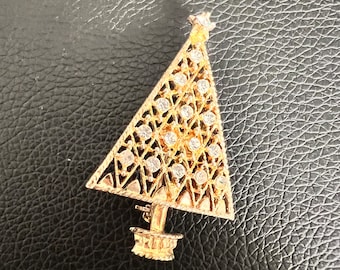 May include: A gold-tone Christmas tree brooch with clear rhinestones. The tree is decorated with a geometric pattern and has a star at the top.